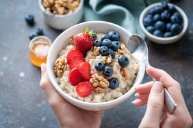 Bowl of oatmeal with fruits and nuts in person's hands