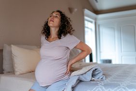 Pregnant woman getting up out of bed and holding her lower back