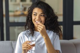 A woman takes a supplement with a glass of water