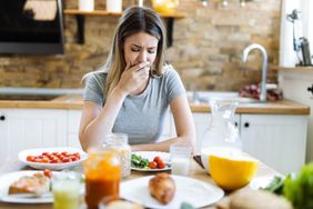 Young woman feeling nausea during breakfast time at dining table