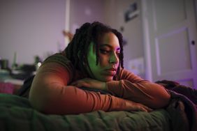 A person lies on their bed with a blank expression