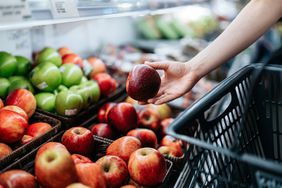 Close up of a person's hand picking up an apple in the produce section of the grocery store.