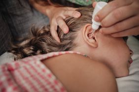 A parent puts ear drops in a little girl's ear