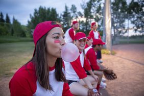 Female softball player blowing bubble gum bubble on bench