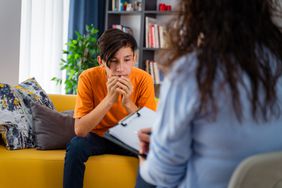 young man looking sad while sitting on a yellow couch in a therapist's office