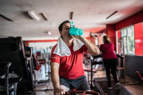 Middle-aged person on gym bike drinking creatine supplement