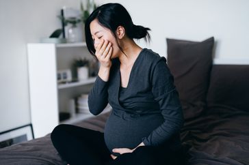 A pregnant woman covers her mouth while regurgitating