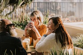 Three colleagues sit outside on a sunny day and enjoy a take-out lunch and coffee