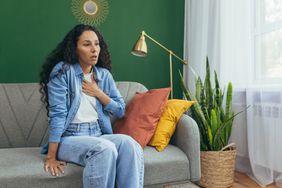 Woman holding her chest while sitting in the couch