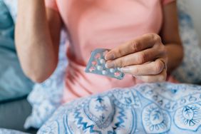 Woman holding pills while in bed.