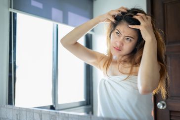 A woman scratches her scalp in the mirror