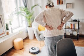 older adult standing in living room and holding lower back in pain