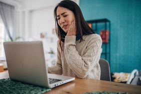 Person with tooth pain holding jaw while working at desk computer