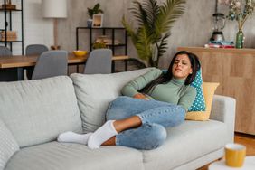 Person laying on the couch in discomfort holding their stomach.