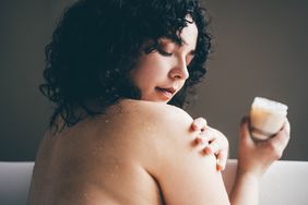 A woman applies cream to her skin in the tub