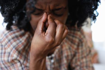 Close-up of a person with a headache, pinching their nose in pain. 