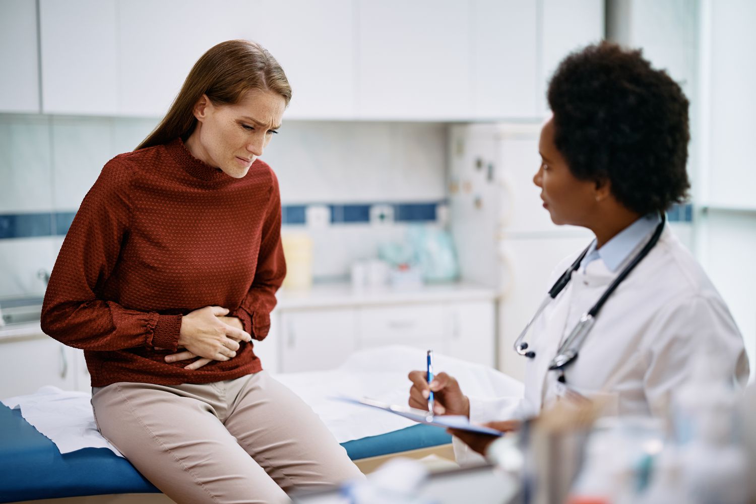 Patient holding abdomen in pain while talking to doctor at medical clinic