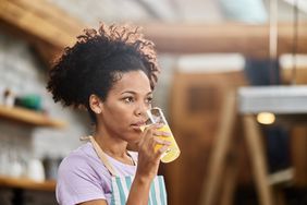 Person drinking orange juice in the kitchen. 