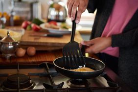 Close-up of a young woman turning eggs with a spatula, frying in a pan.
