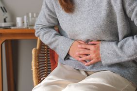 A person has her hands over her belly in pain