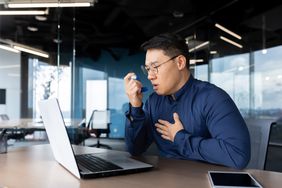 Adult using inhaler for asthma at work, in front of a computer