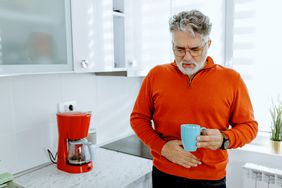 older man holding stomach due to gas after drinking a cup of coffee in the kitchen