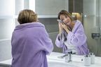 Older person cleans their face in the bathroom.
