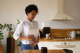 Person with pelvic/cervix pain holding hands on stomach in the kitchen