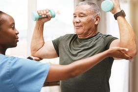 An older man lifts weights with the help of a physical therapist