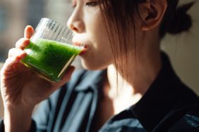 Parasite cleanse: Young Asian woman is drinking a glass of green juice; natural sunlight coming in. 