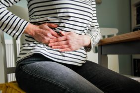 A person sits on a chair while holding their hands to the lower right side of their belly