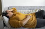 Person lays on the couch holding their abdomen in pain. 