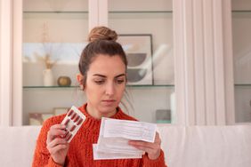 Person holds up medication and reads instructions before taking pills. 