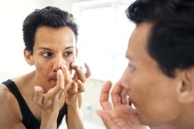 A person analyzes the outside of their nose in the mirror