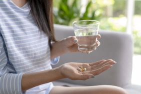 A woman holds supplements in one hand and a glass of water in the other hand