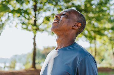 An older man takes a deep breath of fresh air while outside