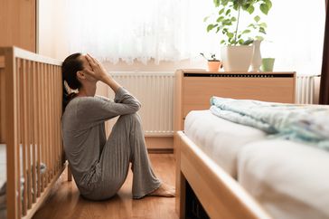 Stressed parent sitting on the floor near crib