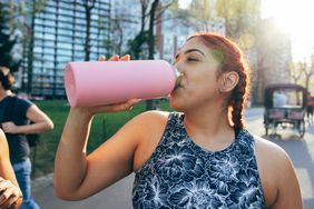 Young woman with braids and wearing a floral athletic top drinking from a metal water bottle
