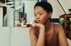 Person sitting on couch with head on hand, looking like they're thinking or upset.