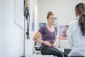 Adult holding her stomach and talking to doctor at medical appointment.