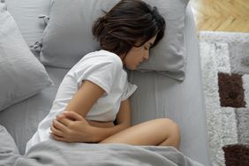 Woman laying in bed holding stomach. 