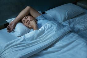 Senior Asian man sleeping with one hand on his chin and his arm across his forehead.