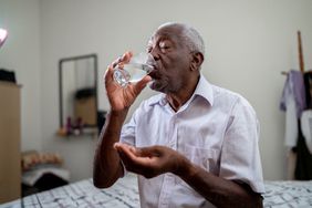 An older man drinks a glass of water as he takes supplements