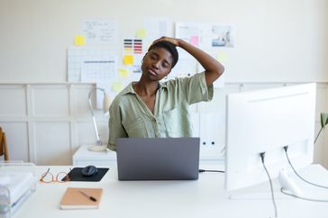 Tired freelancer stretching her neck at her desk.