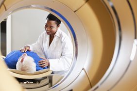 radiologist lightly pressing on the chest of an old man in a blue shirt lying down on an exam table before entering a pet scan machine