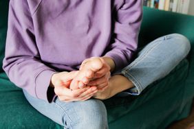 A person sits on the couch and looks at the bottom of their foot