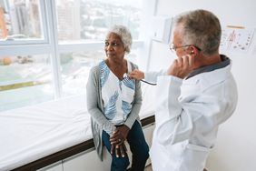 doctor using a stethoscope to listen to older woman's heartbeat while she sits on a hospital bed
