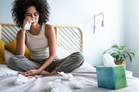 Person in bed with a cold blowing their nose with tissues.