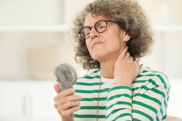 An older woman cools off with a portable fan