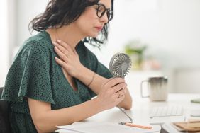 A woman uses a personal fan to cool down while sitting at a desk